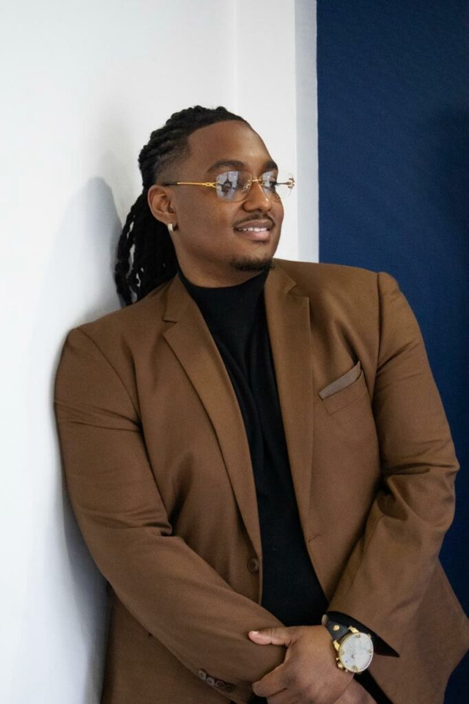 Carlito Henry en blazer brun, posture confiante, lumière naturelle
