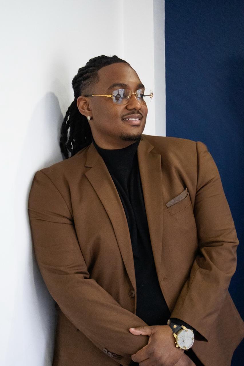 Carlito Henry en blazer brun, posture confiante, lumière naturelle